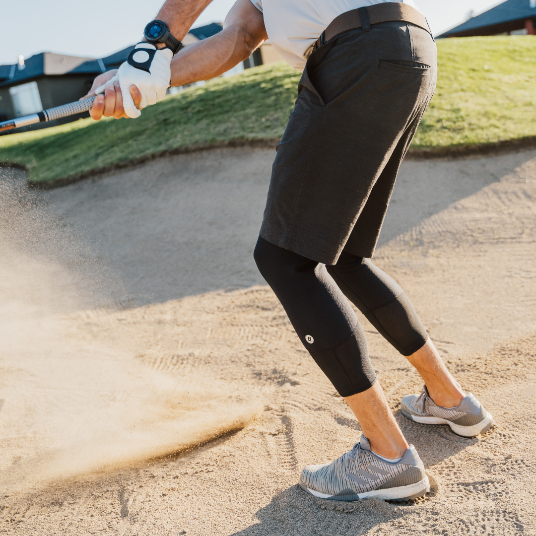 It's hard to dread chipping out of a sand trap when a golf game is supported by Bracelayer! In this photo, a man chips out of a sand trap with knees slightly bent in good golfing form, wearing Bracelayer's KS1 Vent knee stabilizing compression pants.