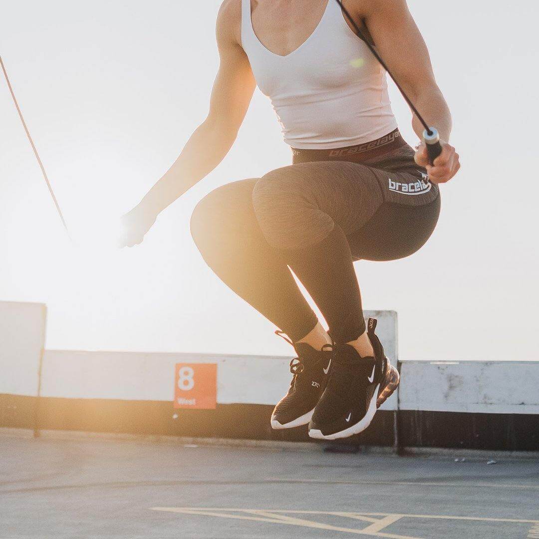 A woman jumps rope in Bracelayer's compression tights for women with a gorgeous sunset in the background. These compression tights for ladies are truly unique due to their knee support layer. 